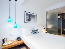 Ein modernes Hotelzimmer mit einem ordentlich bezogenen Bett, einem Nachttisch mit Telefon und Wasserkocher sowie einem gerahmten Bild an der Wand.