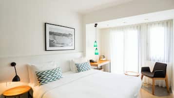 Ein Hotelzimmer mit einem großen Bett, einem Schreibtisch mit Lampe, einem Sessel und einem Fenster mit Vorhängen.