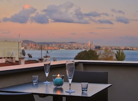 Ein Tisch mit zwei Gläsern und einer Kerze auf einem Balkon mit Blick auf eine Stadtlandschaft bei Sonnenuntergang.