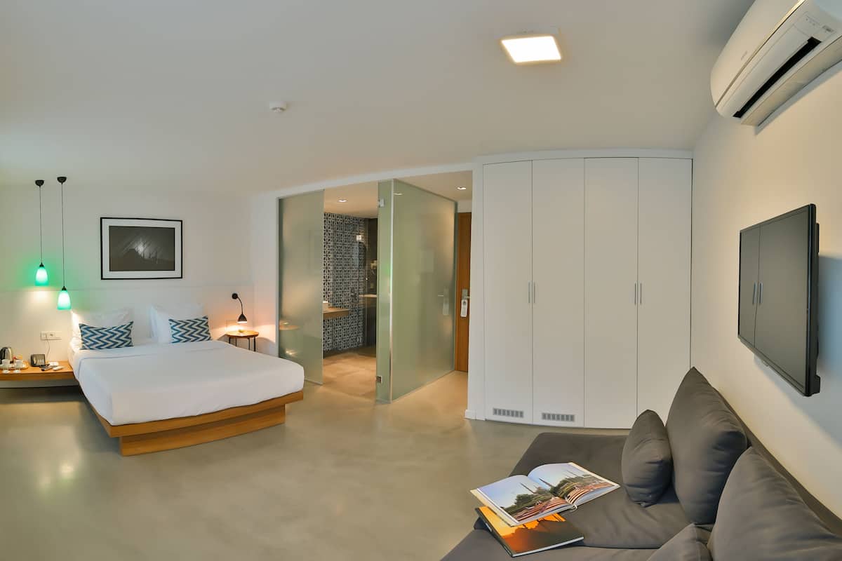 A modern hotel room with a bed, a sofa, a TV, and a sliding door leading to a bathroom.