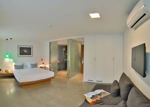 Ein modernes Hotelzimmer mit Bett, Sofa, Fernseher und einer Schiebetür zu einem Badezimmer.