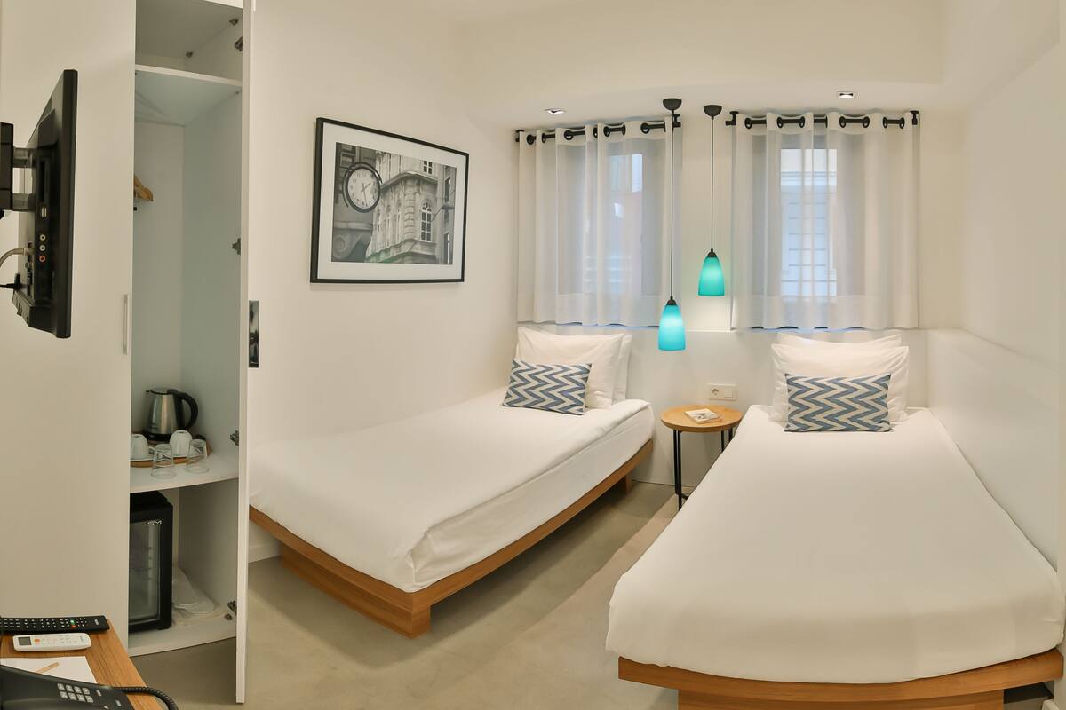 A hotel room with two single beds, a desk with a telephone, a coffee machine, and a framed picture on the wall.