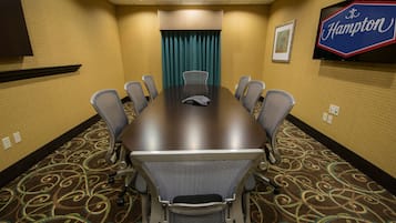 A conference room with a large table, eight chairs, a TV screen, and a Hampton sign on the wall.
