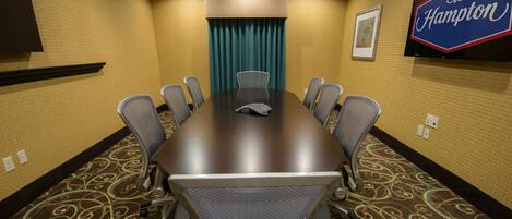 A conference room with a large table, eight chairs, a TV screen, and a Hampton sign on the wall.