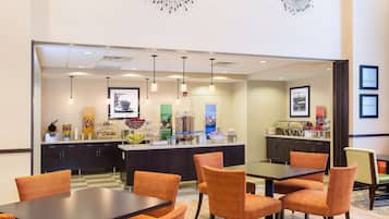 Ein Hotel-Speisebereich mit einem Buffet, orangefarbenen Sitzgelegenheiten und Pendelleuchten.