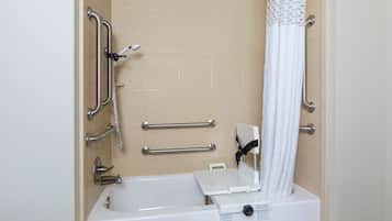 Un baño con bañera, barras de apoyo, un asiento para ducha y una cortina blanca.