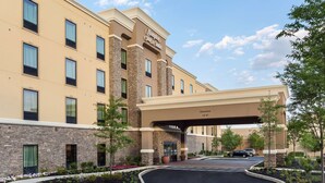 Edifício do Hampton Inn Suites com entrada acessível, fachada de pedra e área de estacionamento com jardim ajardinado.