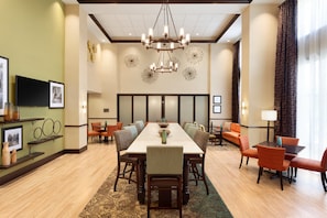A hotel dining area with a long table, multiple chairs, a chandelier, and a television on the wall. - Hampton Inn & Suites Philadelphia Montgomeryville (North Wales)