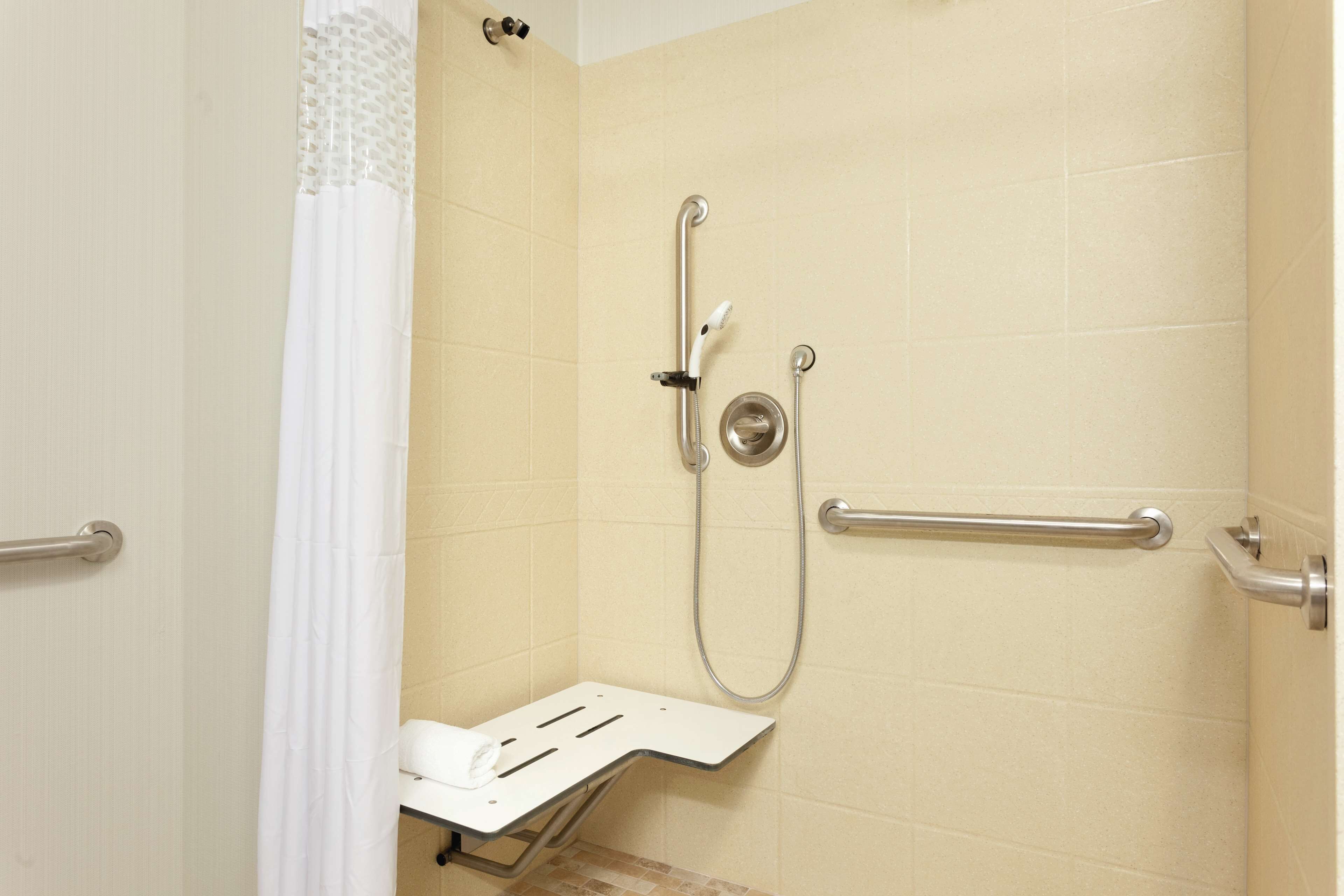 A shower area with a grab bar, a handheld showerhead, and a seat.