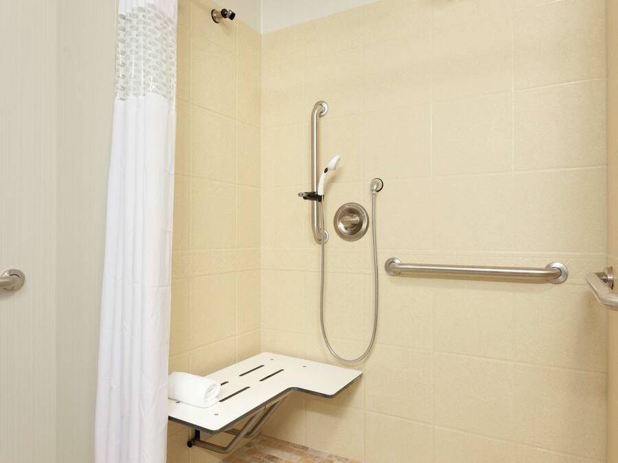 A shower area with a grab bar, a handheld showerhead, and a seat.