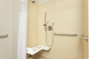Zona de ducha con barra de apoyo, cabezal de ducha de mano y asiento.