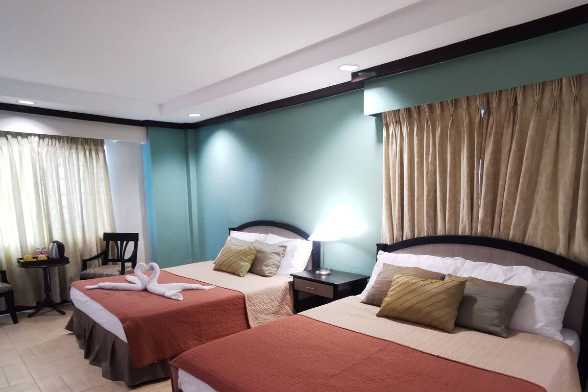 Quarto de hotel com duas camas, uma mesinha e uma cadeira.