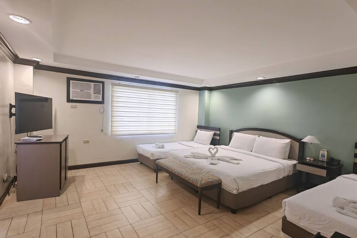 Quarto de hotel com duas camas, televisão, escrivaninha e janela com persianas.