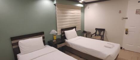 A hotel room with two beds, a small table, a chair, and a door.