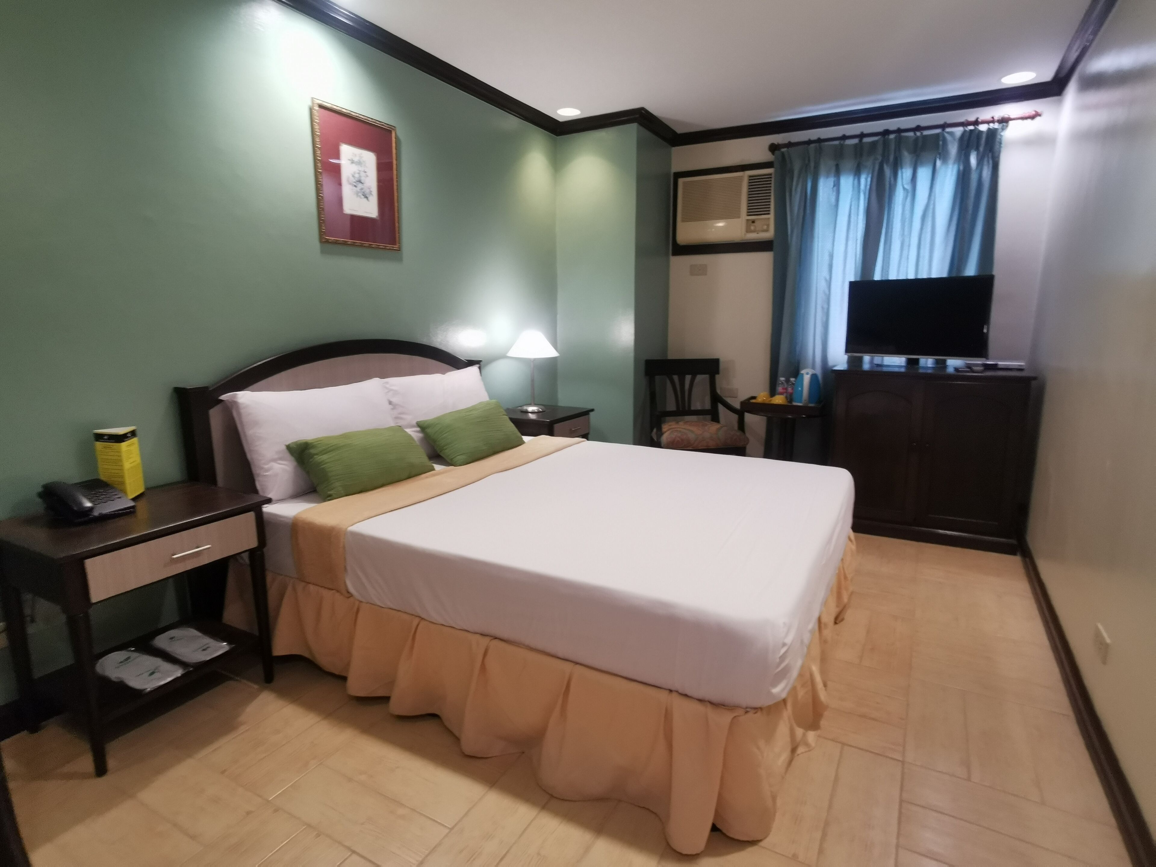 Habitación de hotel con cama, mesita de noche, lámpara, silla, televisión y aire acondicionado.