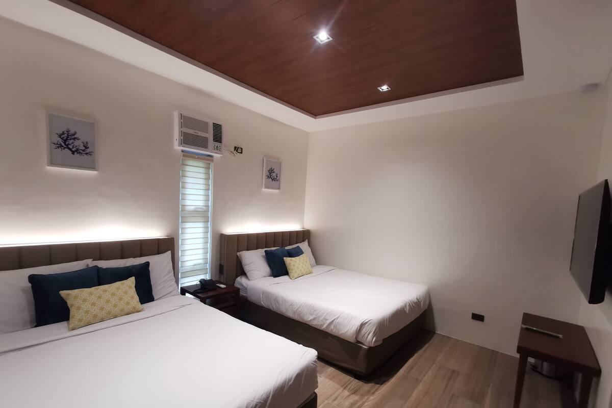 Quarto de hotel com duas camas, teto de madeira e televisão fixada na parede.
