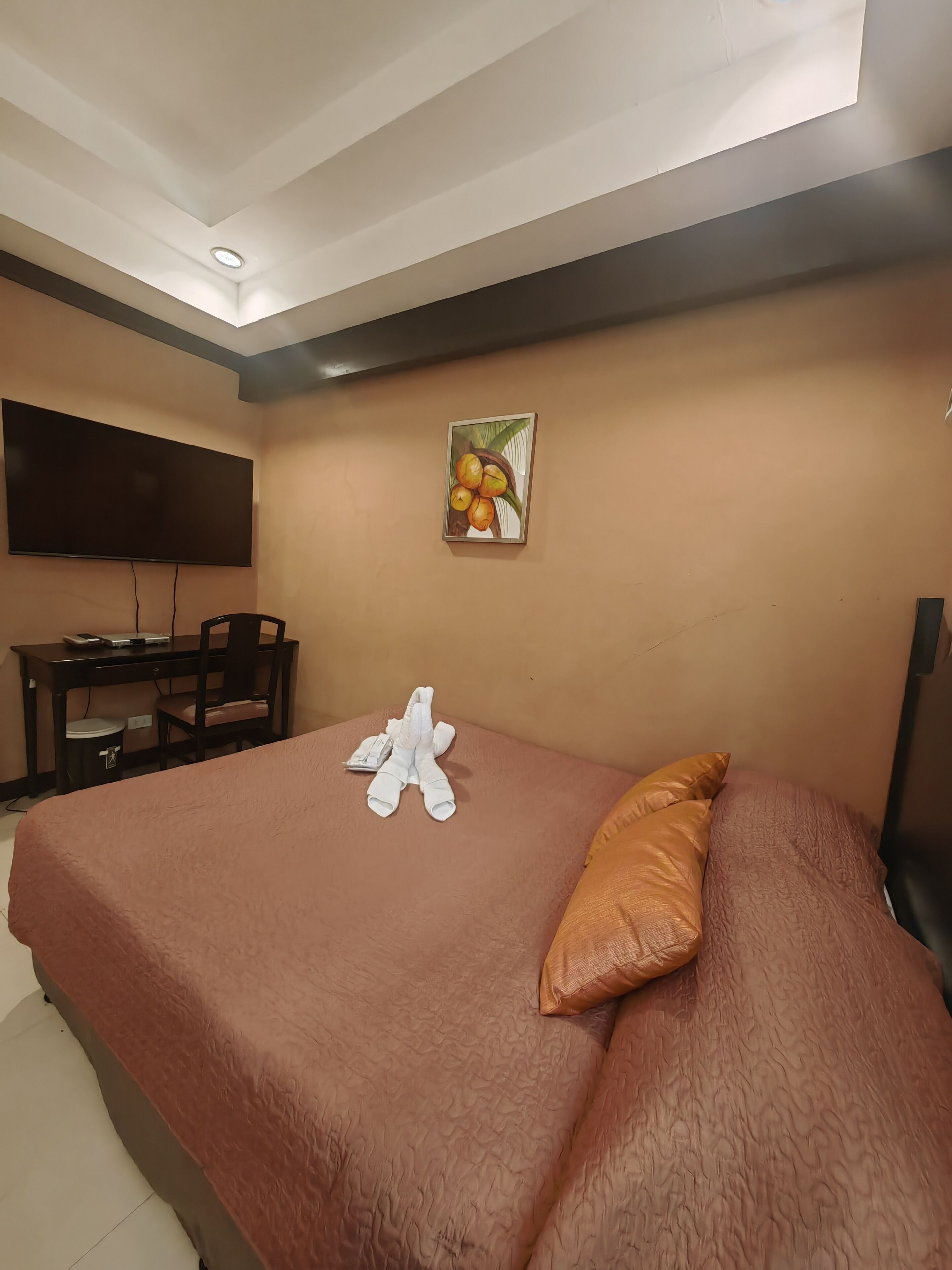 A hotel room with a bed, a desk, a chair, a flat-screen TV, and a painting on the wall.
