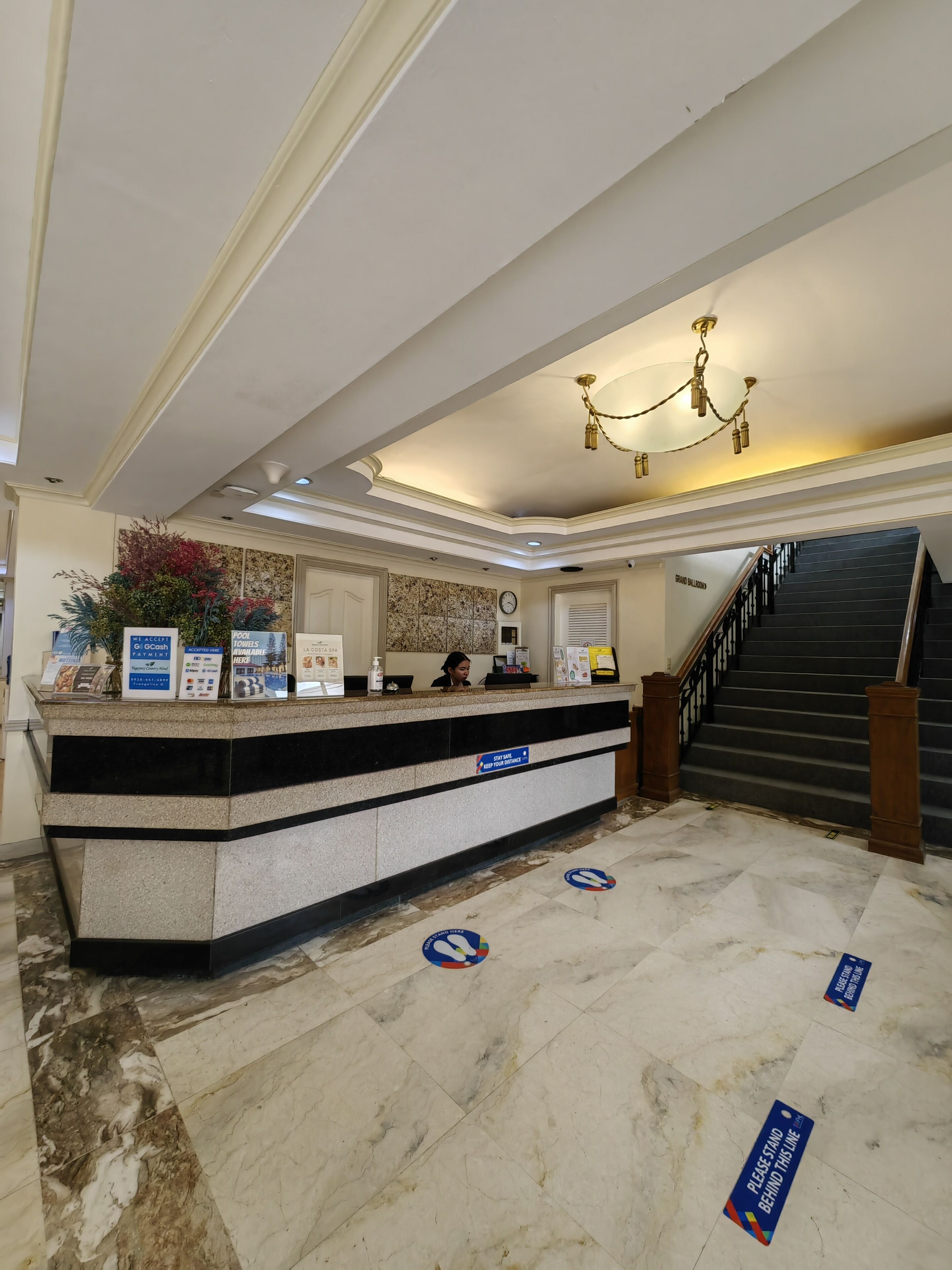 A hotel reception area with a marble floor, a reception desk, a chandelier, and a staircase.