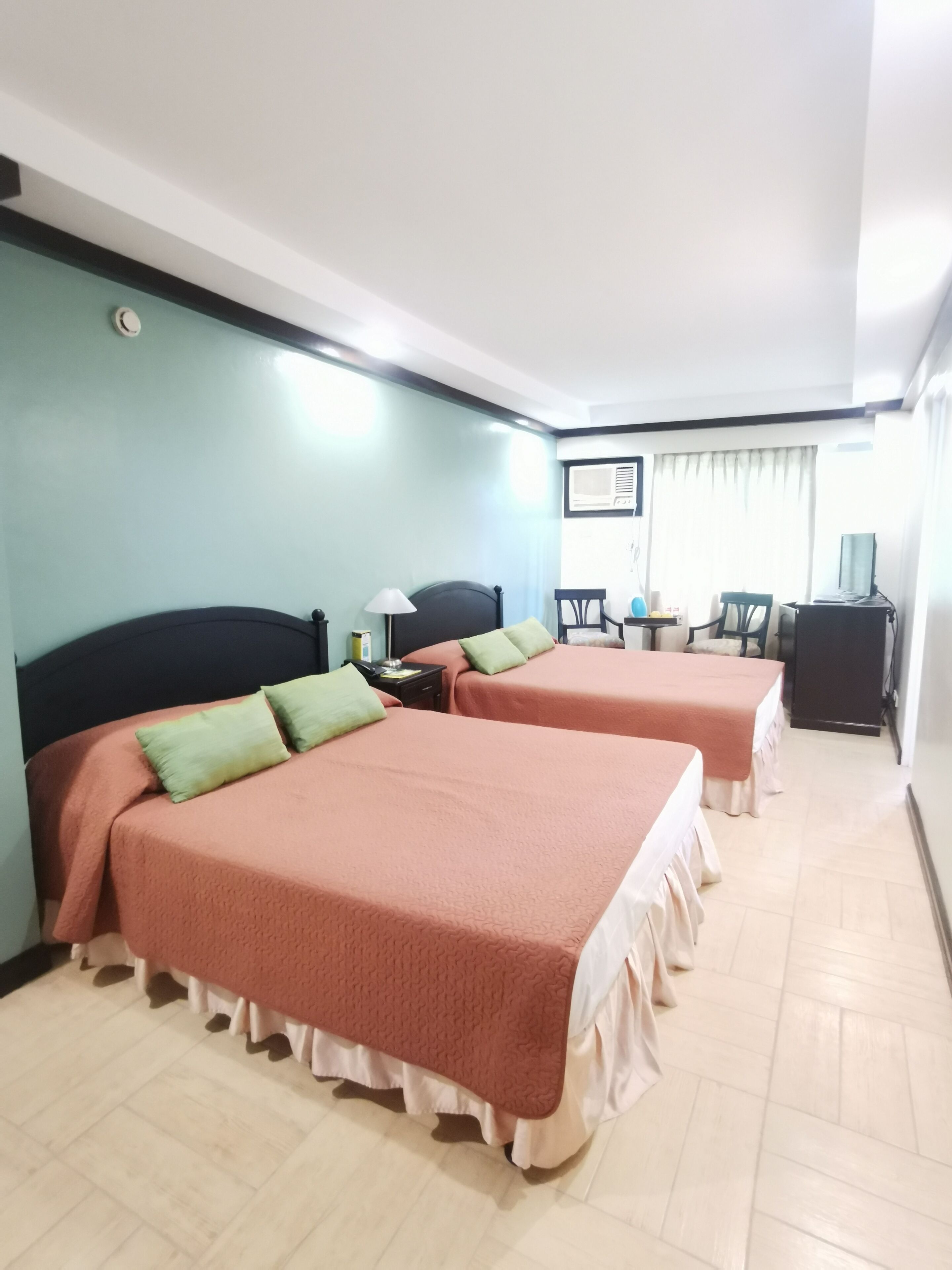 A hotel room with two beds, a desk, a chair, and a television.