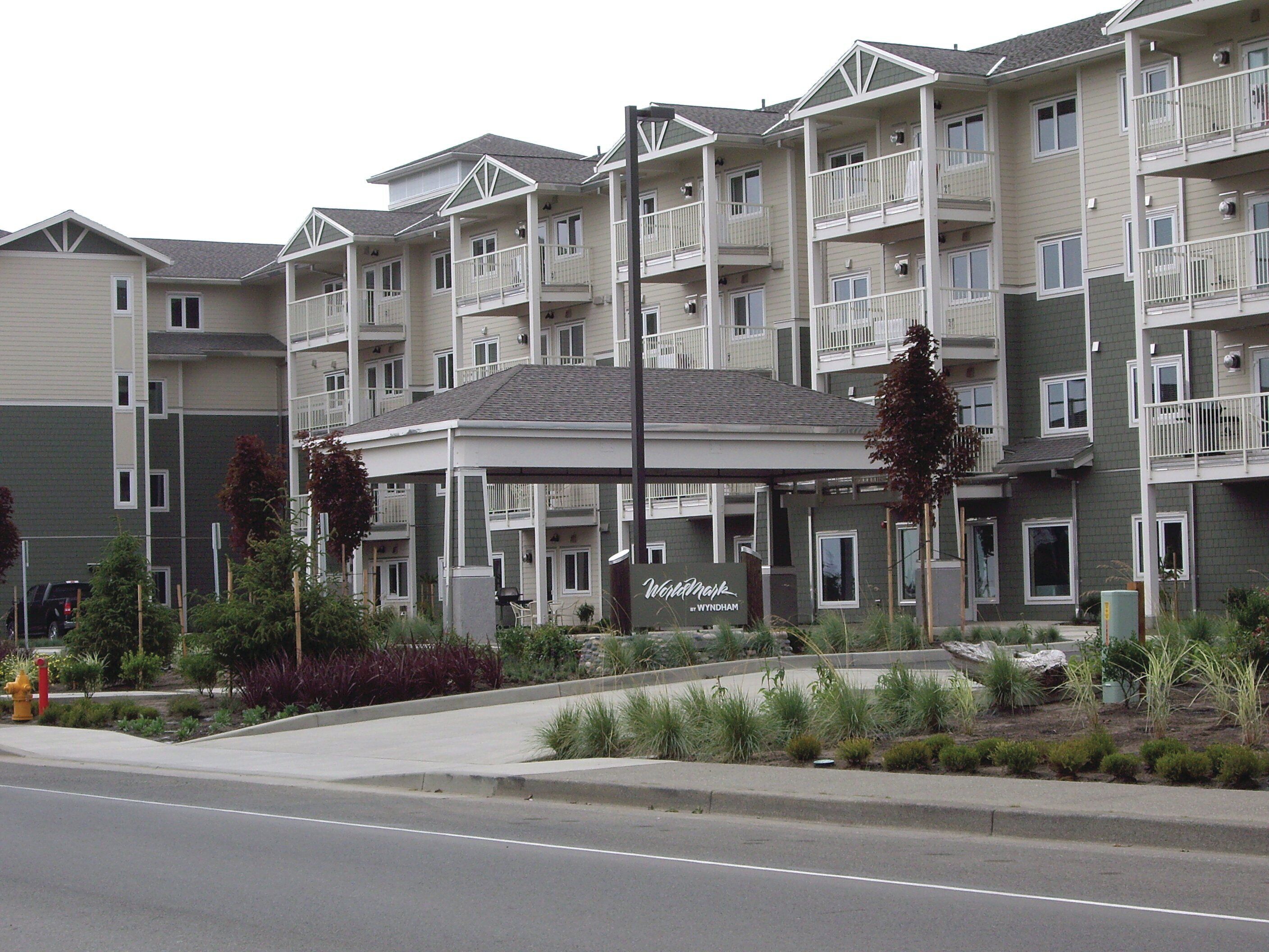 A multi-story hotel with balconies, a covered entrance, and a landscaped area with plants.