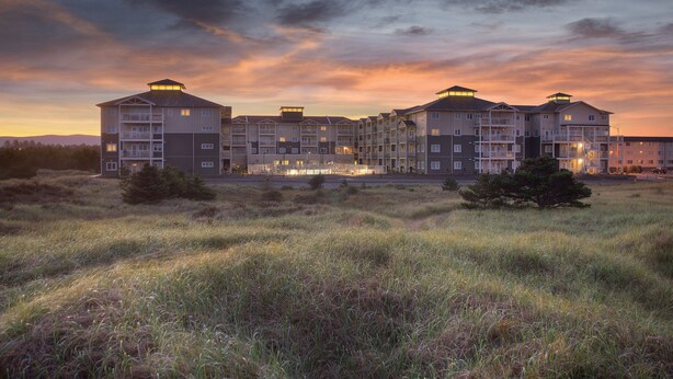 Un hotel de varios pisos con balcones, situado en una zona arbolada bajo un cielo al atardecer.