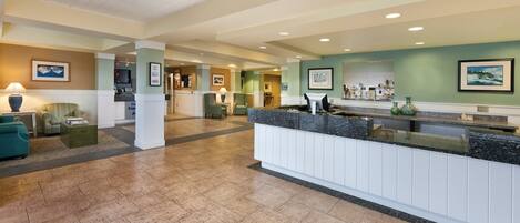 A hotel lobby with a reception desk, seating area, and a hallway leading to other rooms.