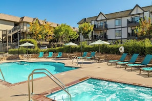 A swimming pool area with lounge chairs and umbrellas, surrounded by buildings with balconies. - WorldMark Solvang (Solvang)