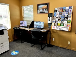 Un espacio de trabajo con dos escritorios, computadoras y un tablón de anuncios con diversos adhesivos y un cartel del Big Bear Visitors Bureau.