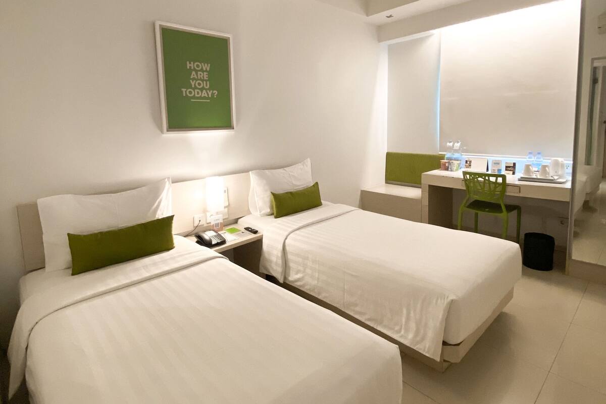 A hotel room with two beds, a desk, a chair, and a window.