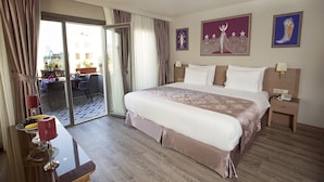A hotel room with a large bed, a bedside table with a lamp, a nightstand, and a view of the outside balcony. - Taximist Hotel (Istanbul)