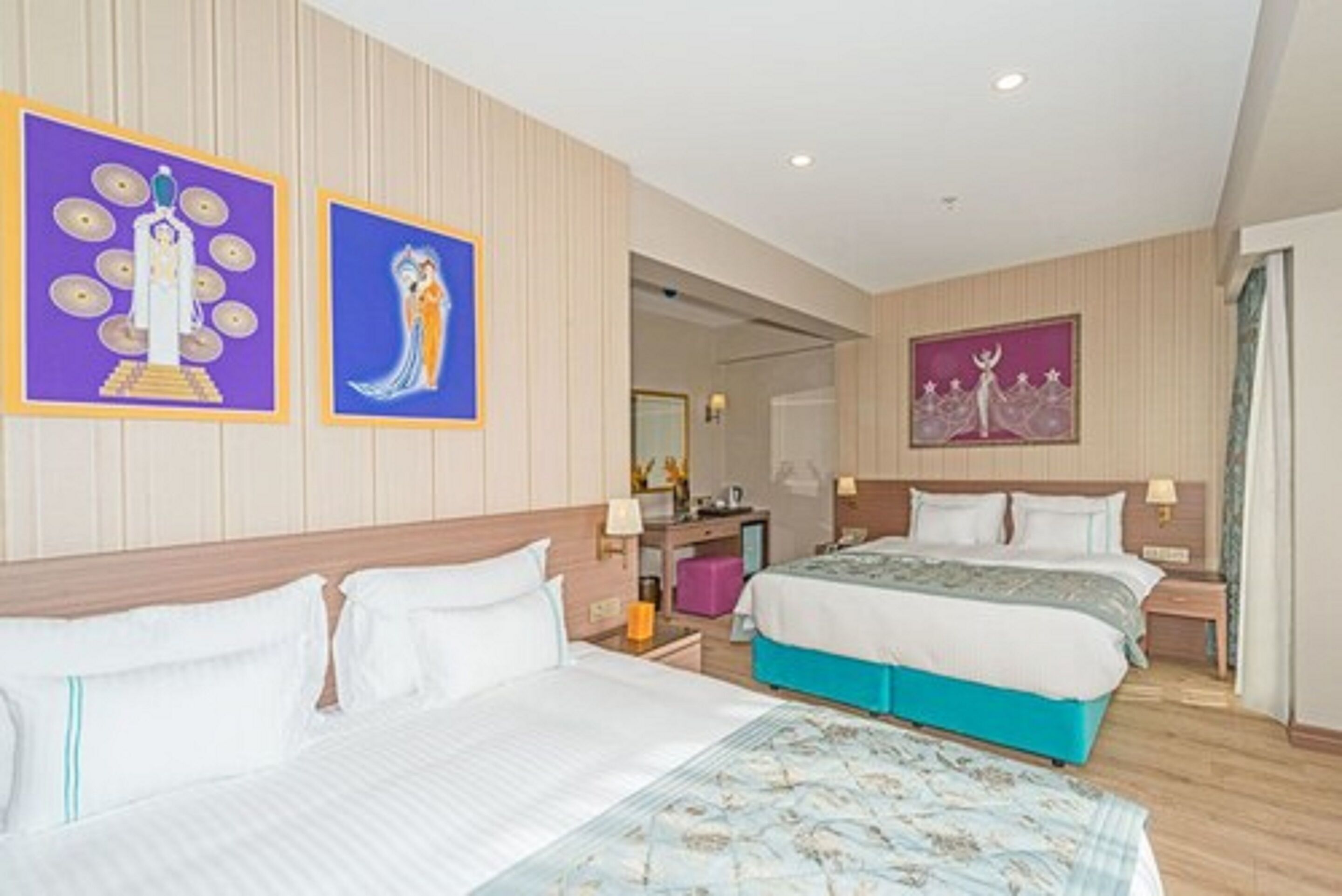A hotel room with two beds, a desk, and artwork on the walls.