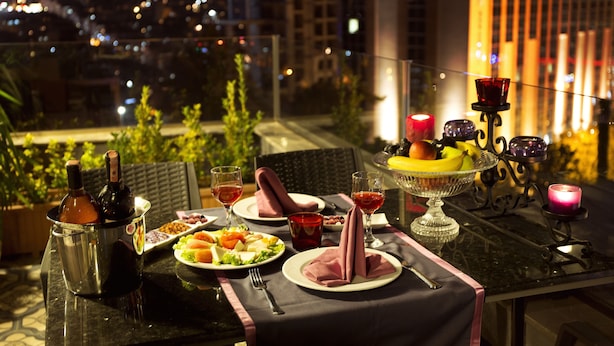 A rooftop dining table set with plates, glasses, and candles, overlooking a cityscape at night. - Taximist Hotel (Istanbul)