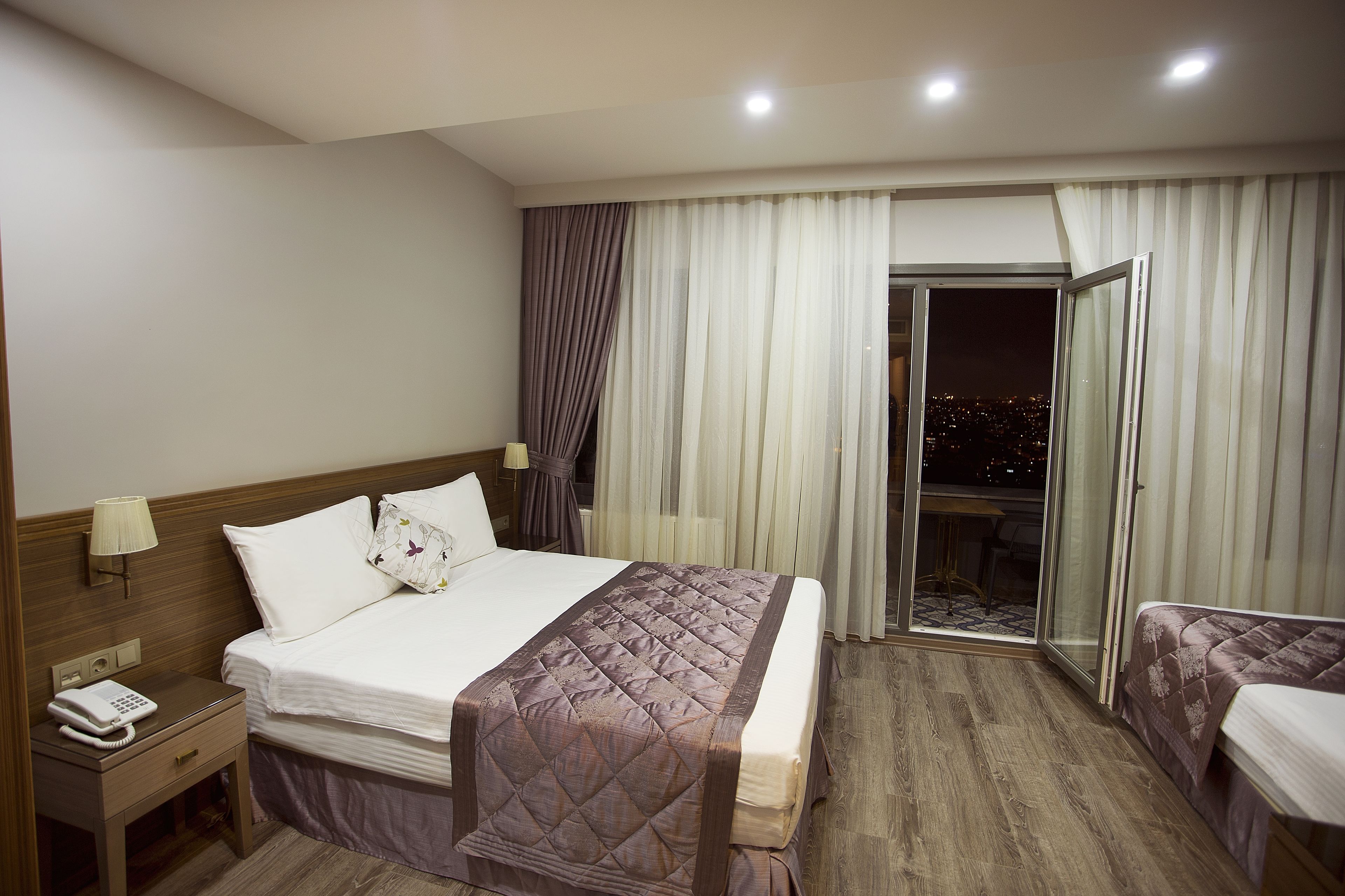 A hotel room with a bed, bedside table, lamp, and a view through a glass door.