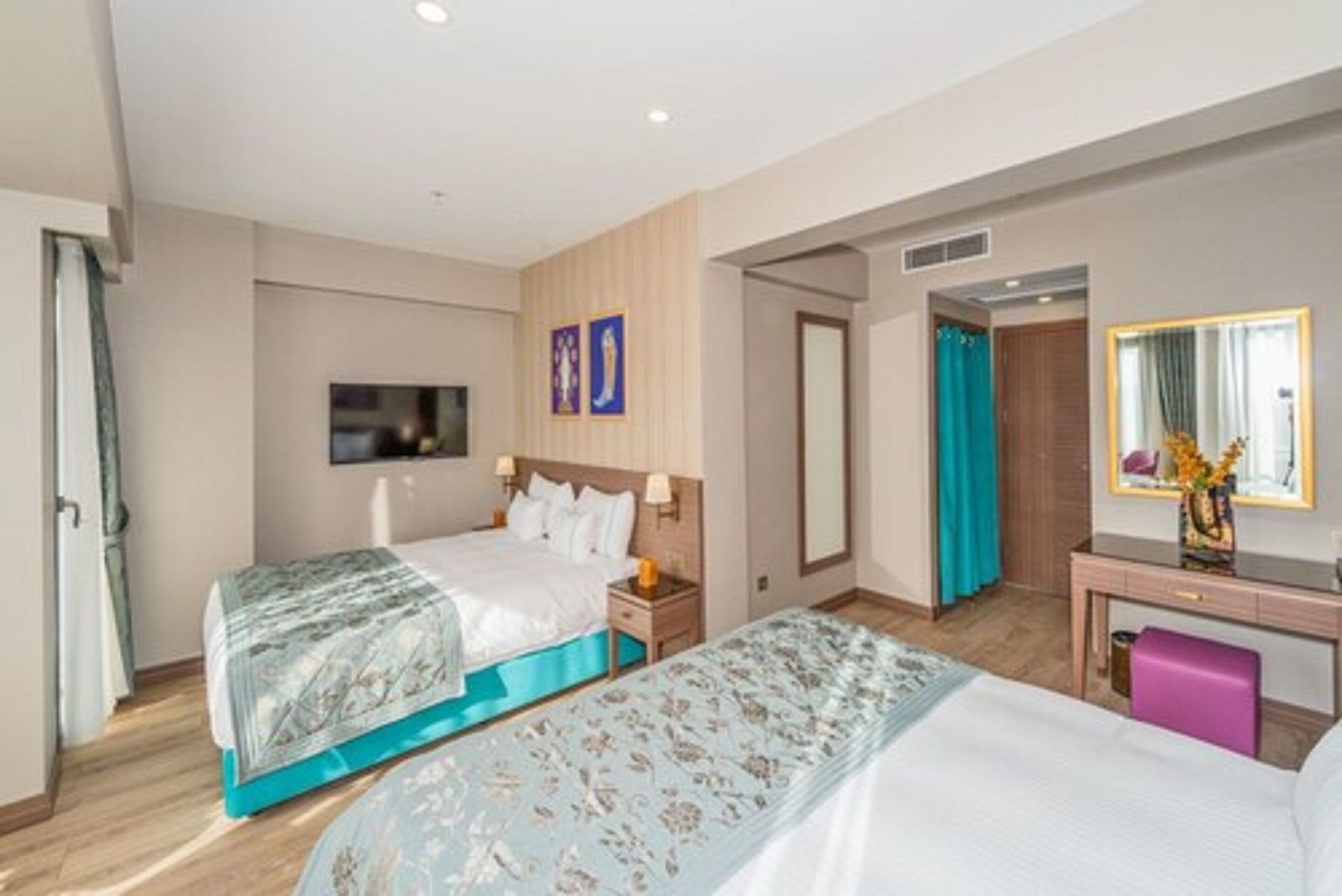 Ein Hotelzimmer mit zwei Betten, einem Fernseher, einem Schreibtisch mit Spiegel und einer Badezimmertür.