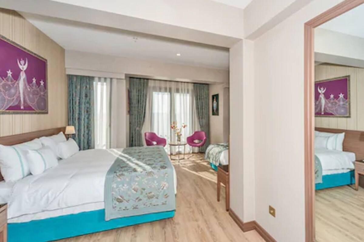 A hotel room with a large bed, a desk, two chairs, and a mirror.