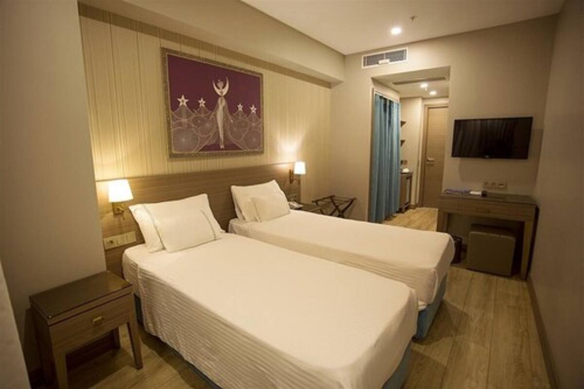 A hotel room with two beds, a TV, a desk, and a painting on the wall.