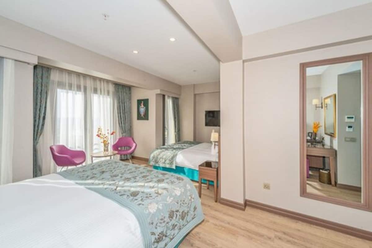 A hotel room with two beds, a large mirror, a desk with a lamp, and a chair.