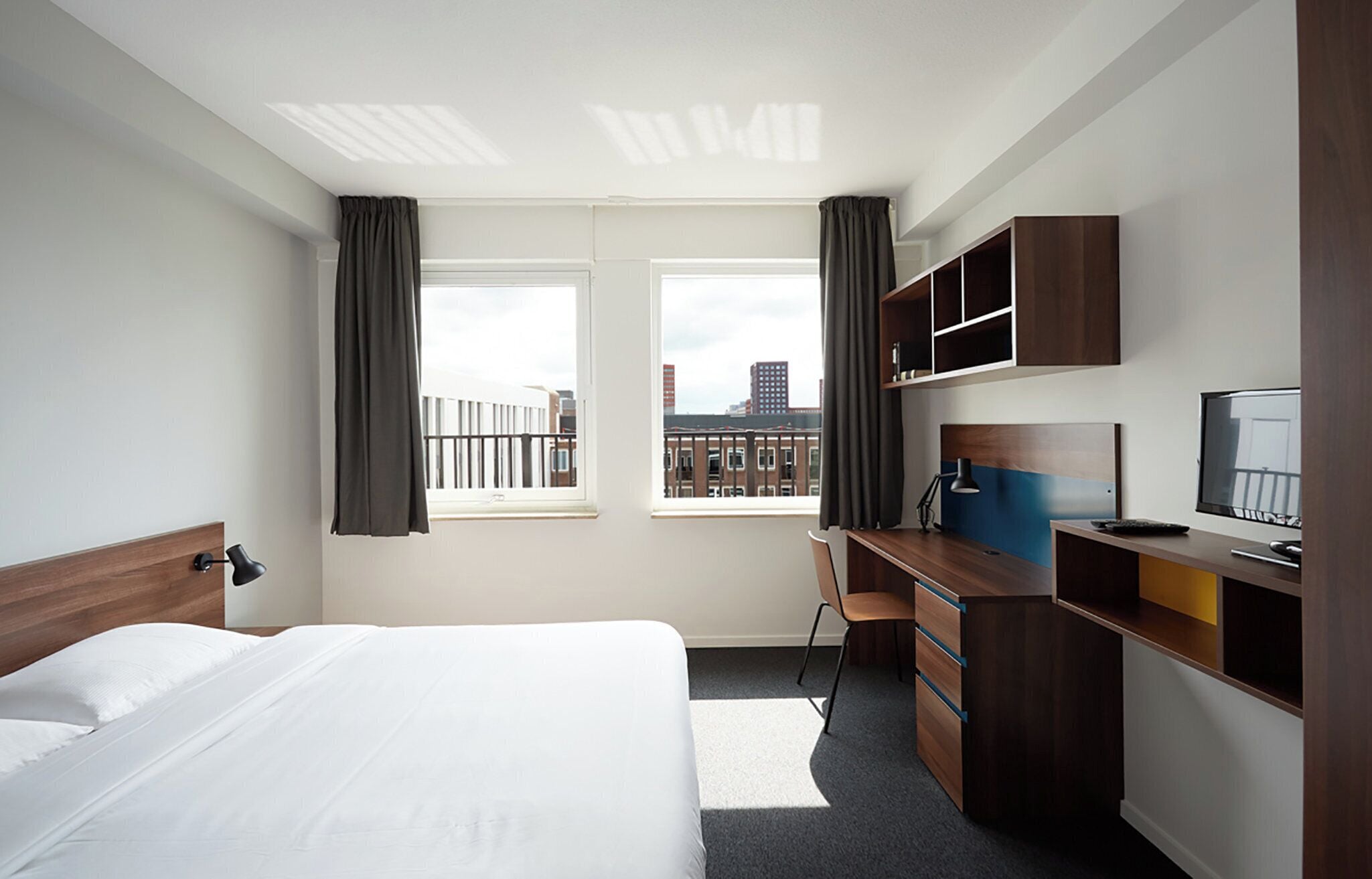 Une chambre d’hôtel avec un lit, un bureau et une vue sur les immeubles par la fenêtre.
