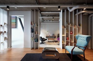 Un interior moderno con piso de madera, un otoman negro, un sillón azul y estanterías llenas de libros.