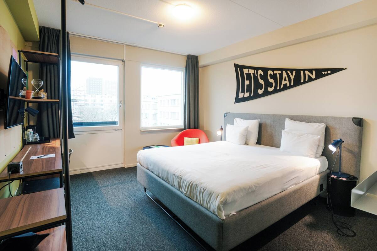 A hotel room with a bed, a desk, a chair, a TV, and a window.