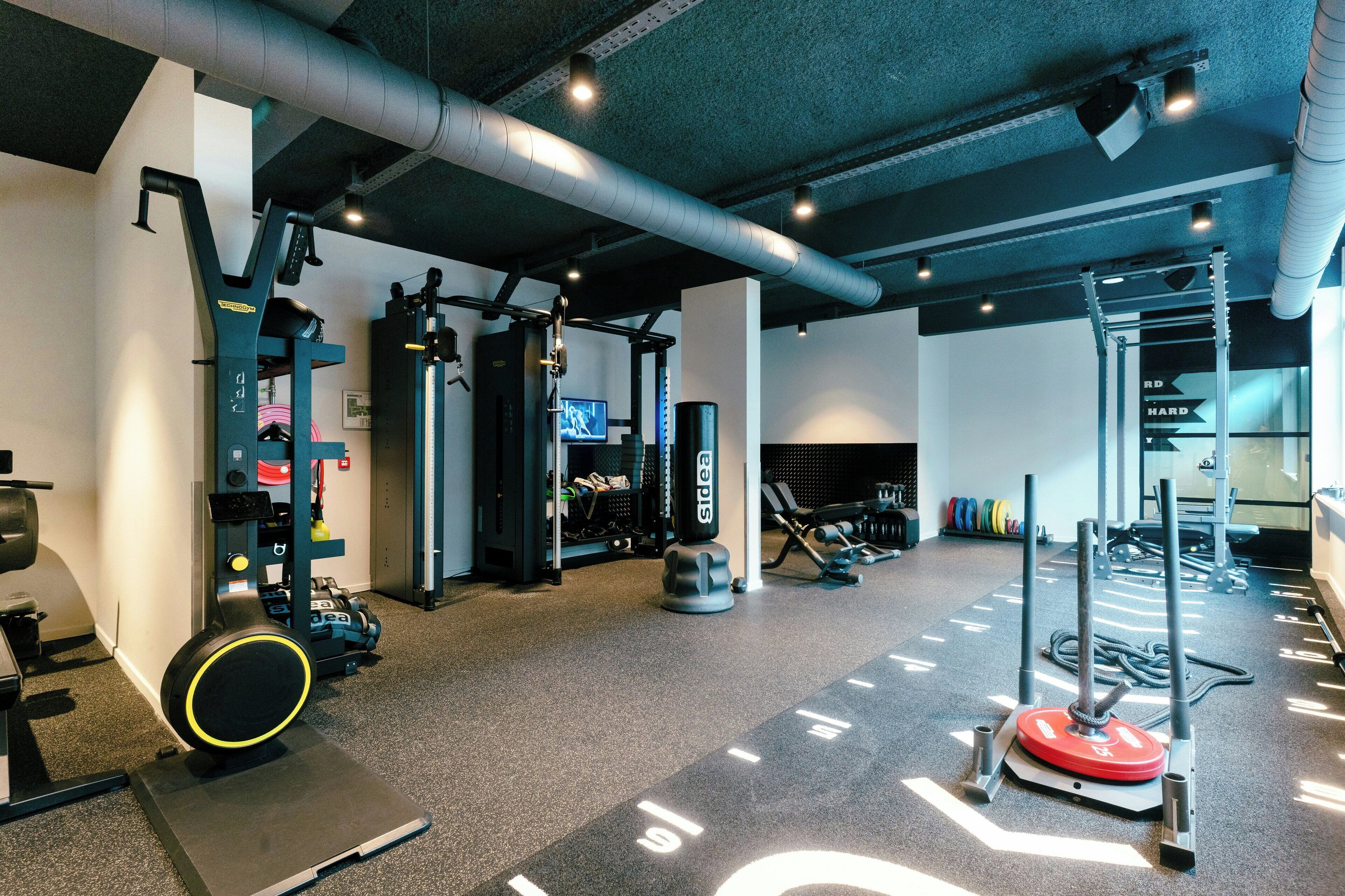 Ein Fitnessstudio mit verschiedenen Trainingsgeräten, darunter Laufband, Kraftgeräte und ein Squat-Rack.