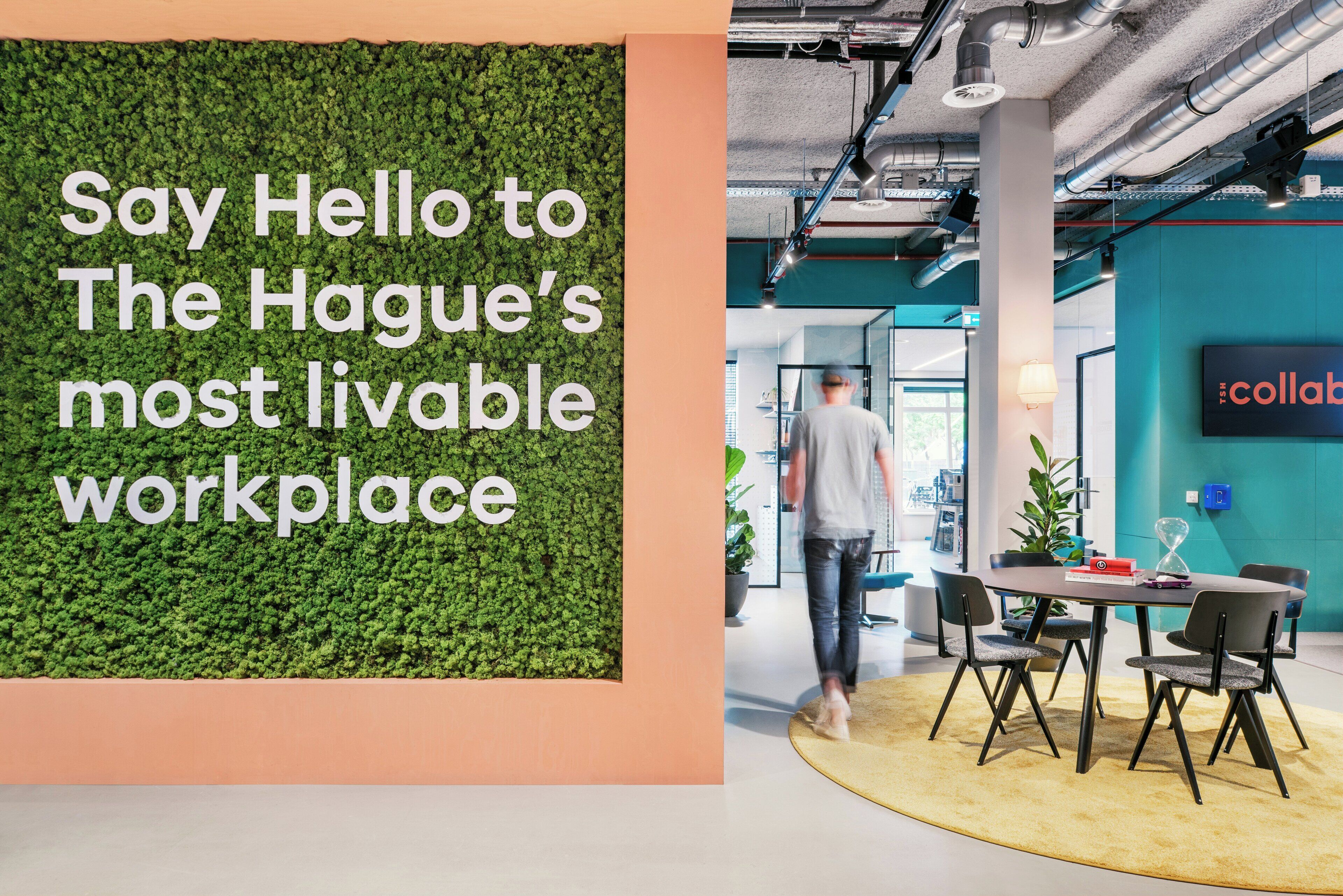 Un espace de bureau moderne avec un mur végétal, des touches de couleur turquoise et une table ronde entourée de chaises.