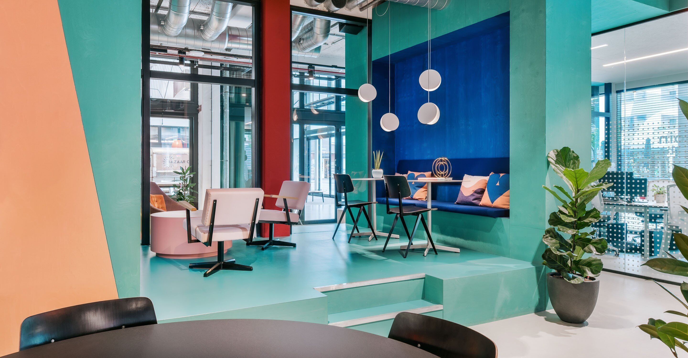Een moderne kantoorruimte met turquoise en oranje wanden, een zithoek met een bank en stoelen, en een potplant.
