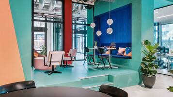 Een moderne kantoorruimte met turquoise en oranje wanden, een zithoek met een bank en stoelen, en een potplant.
