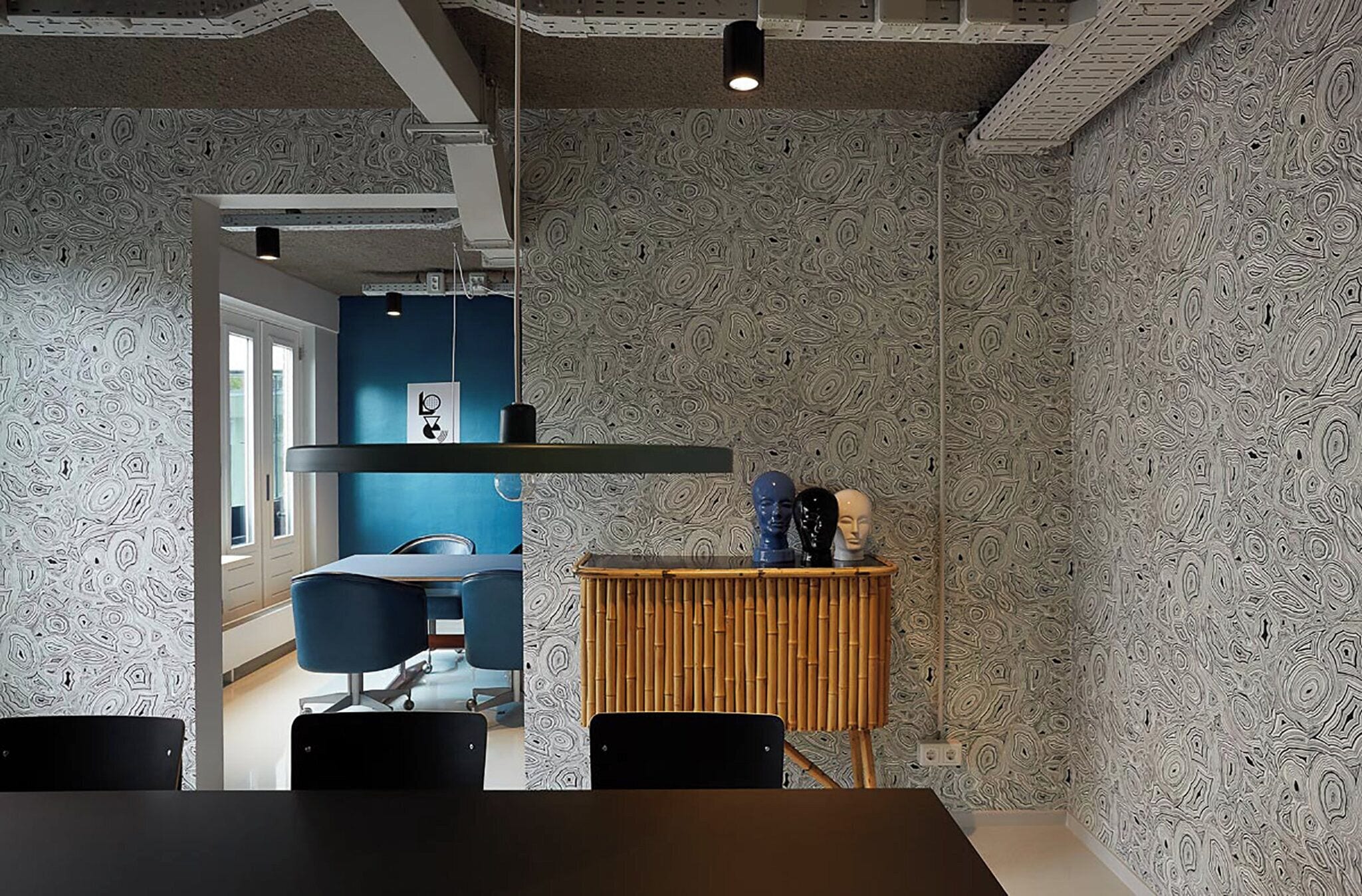 A modern office space with a conference table, chairs, a blue accent wall, and a unique patterned wallpaper.