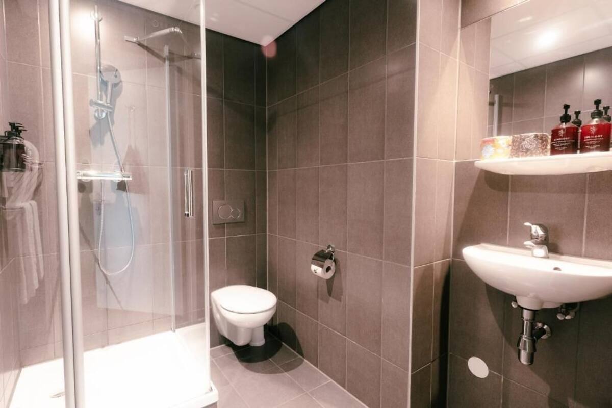A modern bathroom with a glass-enclosed shower, a toilet, and a sink with toiletries on a shelf.