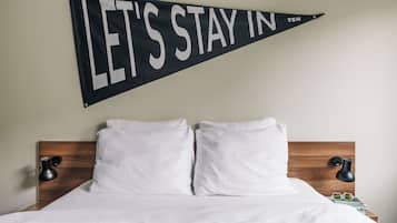 Una cama bien tendida con sábanas blancas, cabecera de madera y dos lámparas de noche. Un banner negro con texto blanco está colgado sobre la cama.