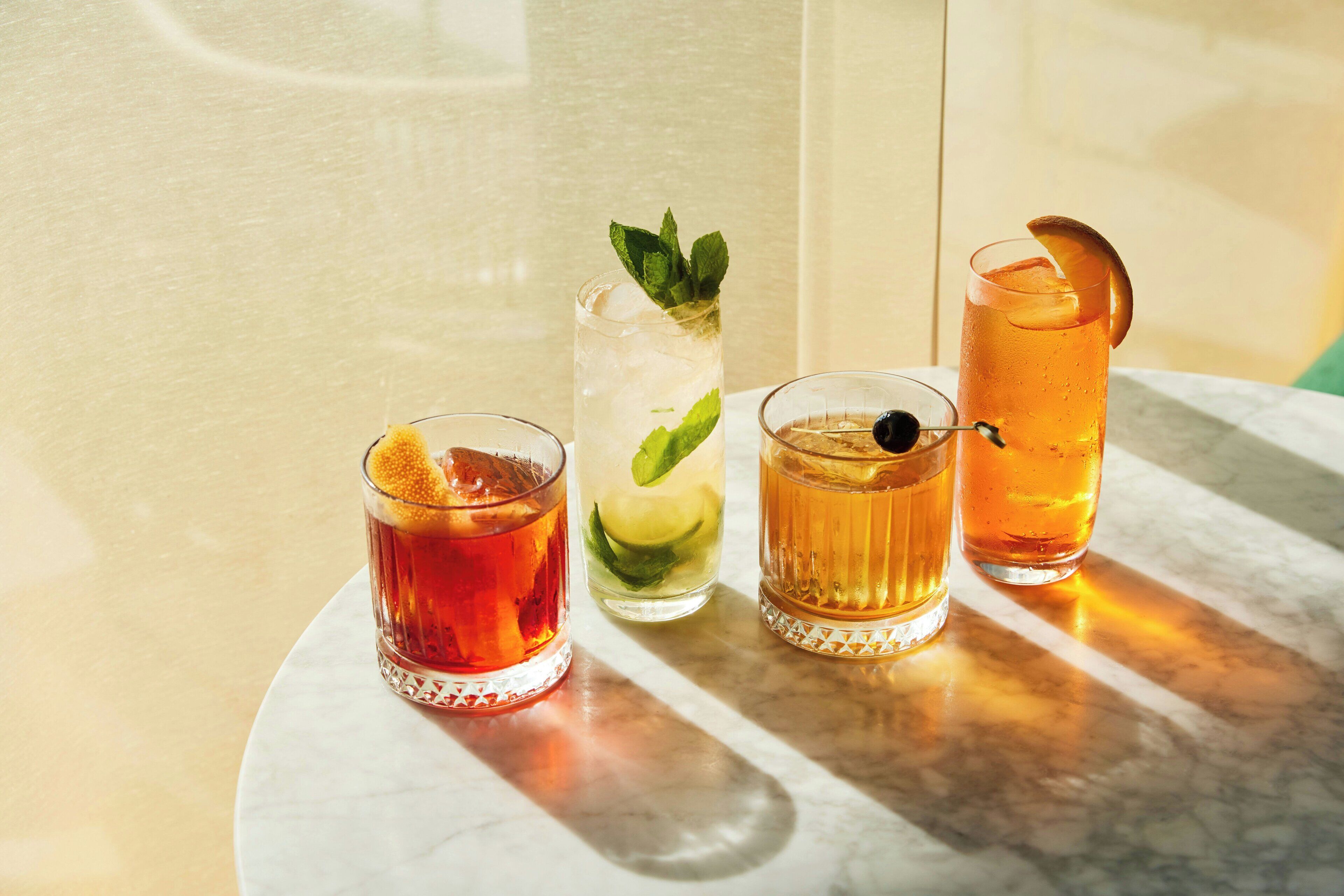 Quatre verres remplis de boissons sont posés sur une table en marbre, avec un mur de couleur claire en arrière-plan.