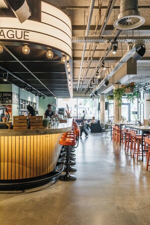 A modern bar area with a curved counter, stools, and a visible menu board. - The Social Hub The Hague (The Hague)