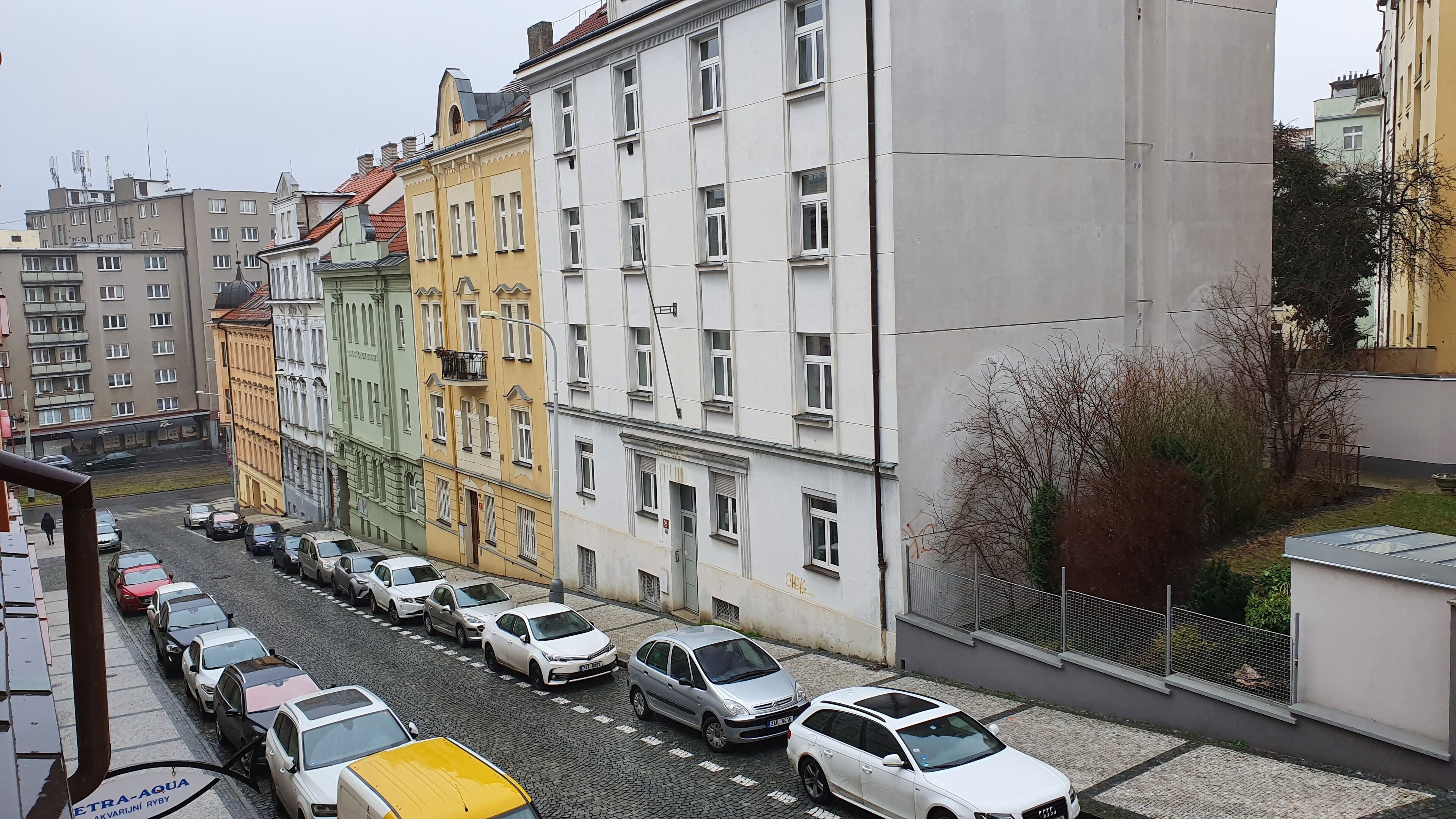 A street view with parked cars and multi-story buildings with various architectural styles.
